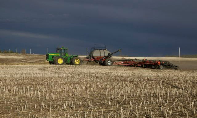 farm tractor seeding under storm clouds